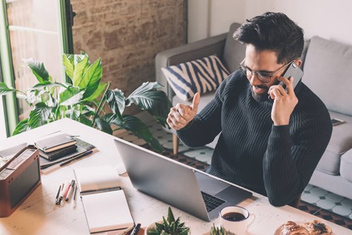man on the phone surrounded by laptop and notes pages 