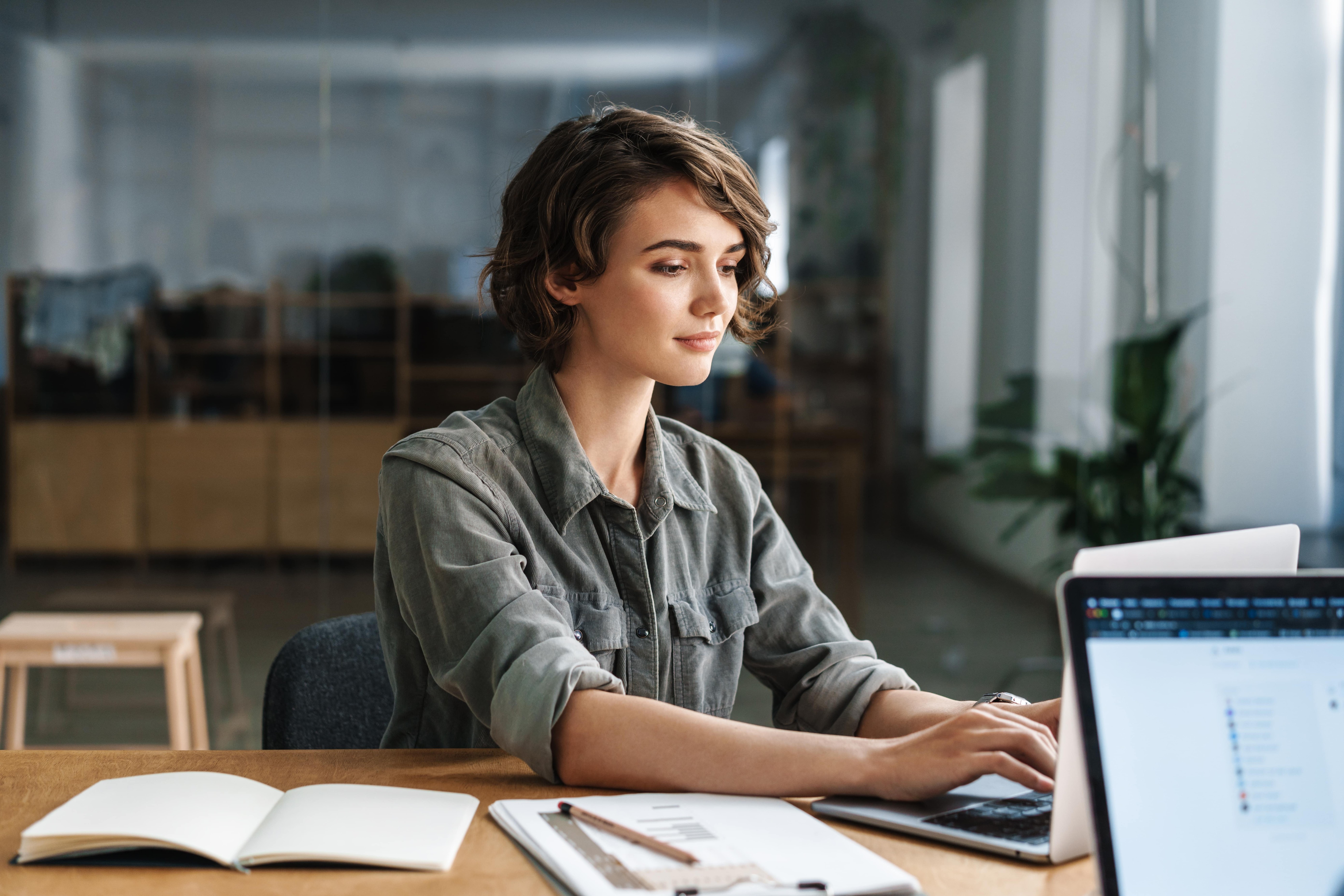 woman typing at laptop with work notes surrounding her 