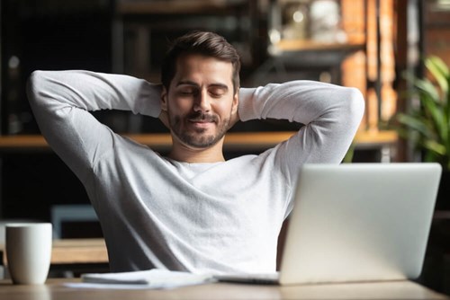 Man leaning back and relaxing at his desk with a laptop
