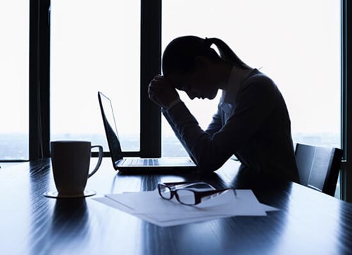Women holding her head in her hands sat in front of computer screen 